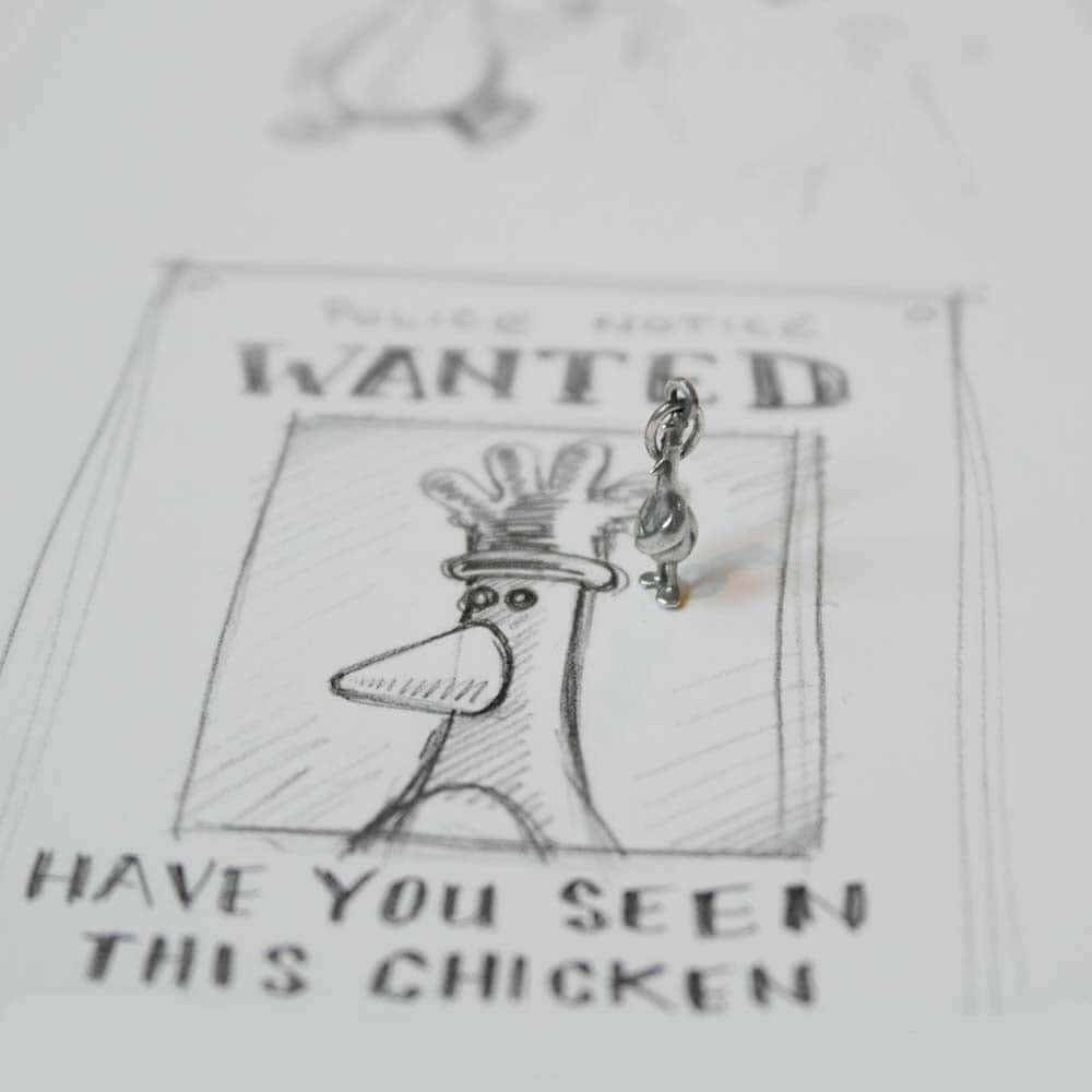 Feathers McGraw sterling silver charm displayed on a Wallace & Gromit-style wanted poster – quirky handmade jewellery inspired by the iconic character.