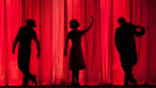 Silhouettes performing on stage behind red theatre curtains for gifts for musical theatre lovers blog