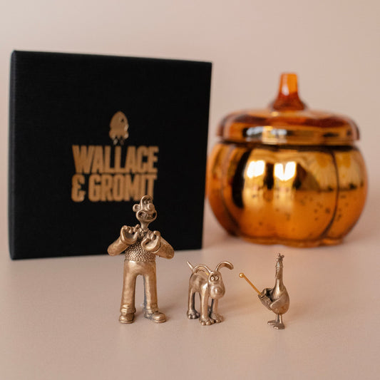 Bronze Wallace & Gromit figurines with Licensed To Charm gift box and orange ceramic jar, celebrating Wrong Trousers Day.