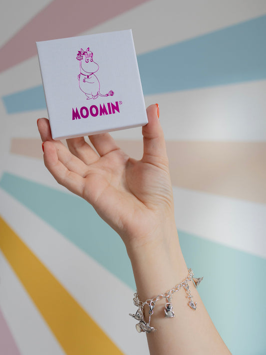 Model’s wrist wearing a silver charm bracelet featuring Moomin characters, styled outdoors
