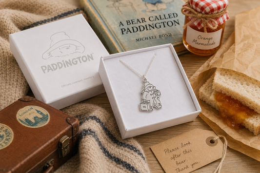 Paddington & Suitcase Sterling Silver Necklace styled with official packaging, marmalade, a vintage suitcase and classic book.