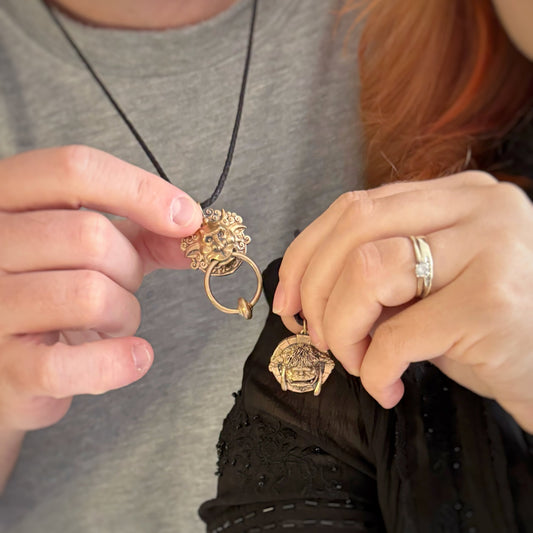 Licensed To Charm model holding the Labyrinth Left Door Knocker and Ludo bronze necklace on an adjustable black cord