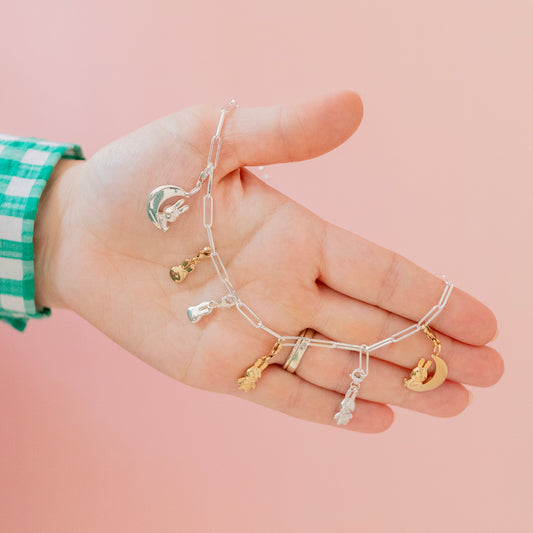 Licensed To Charm Paperclip bracelet with multiple Miffy charms worn on the wrist, photographed against a soft pink background for a playful, collectible look