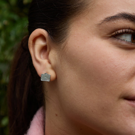 Woman wearing Paddington luggage earrings with bow in sterling silver, close-up on ear