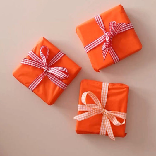 Licensed To Charm orange gift wrapping with red and white checkered ribbons on a beige background