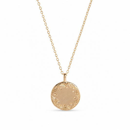 A Frida kahlo gold pendant necklace featuring a round, flat gold disc pendant with a delicate floral border engraving, suspended from a fine gold chain against a solid white background.
