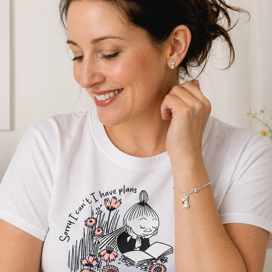 Woman wearing a Moomin graphic T-shirt with sterling silver Moomin bracelet and stud earrings in a soft studio lifestyle setting.