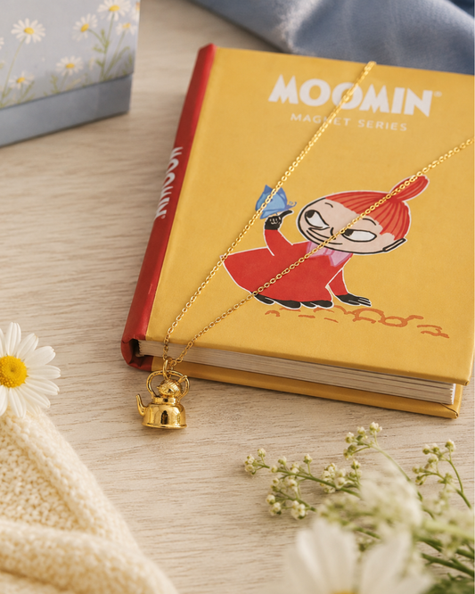 Licensed To Charm officially licensed Moomin jewellery gold vermeil Little My necklace styled with a Moomin book in a soft nostalgic lifestyle setting.
