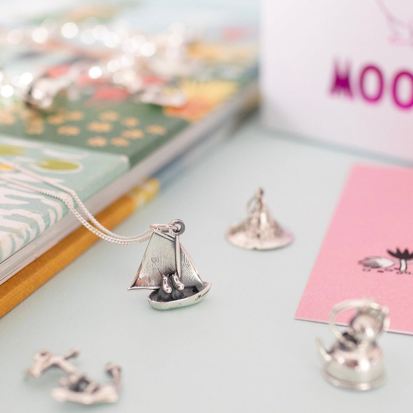 Flat lay of Thingumy & Bob Anchor Charm with polished silver finish, photographed alongside other Moomin jewellery pieces