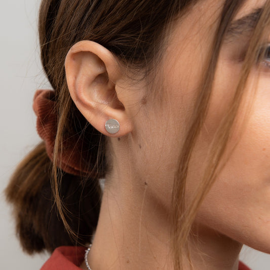 Close-up of the mismatched Amor et Virtute stud earrings highlighting the engraved lettering and gold vermeil shine