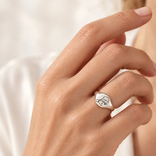 Hand wearing a silver Paddington Bear signet ring with his face engraved beneath his hat.