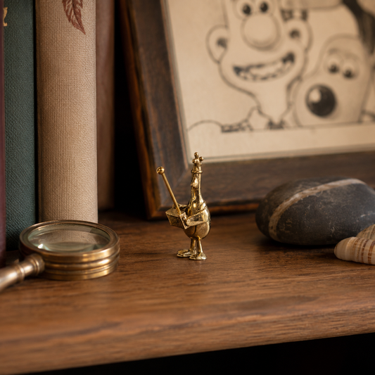 Miniature Wallace & Gromit Feathers McGraw bronze figurine displayed on a wooden shelf beside books, a magnifying glass and collectable home decor.