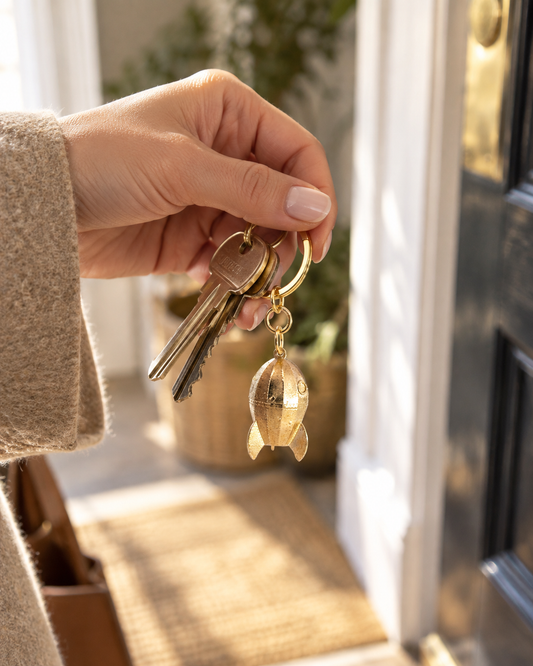 A hand holding a set of keys with a wallace-gromit-rocket-keyring-keys-lifestyle in front of a doorway.