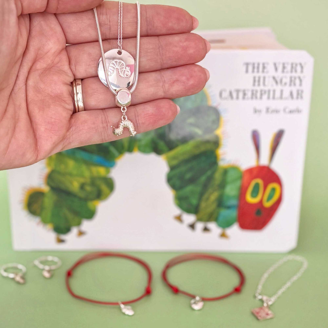 Handmade jewellery pieces from The Very Hungry Caterpillar™ Collection displayed with an open book in the background, evoking a nostalgic, storybook feel perfect for gifting and storytelling moments.