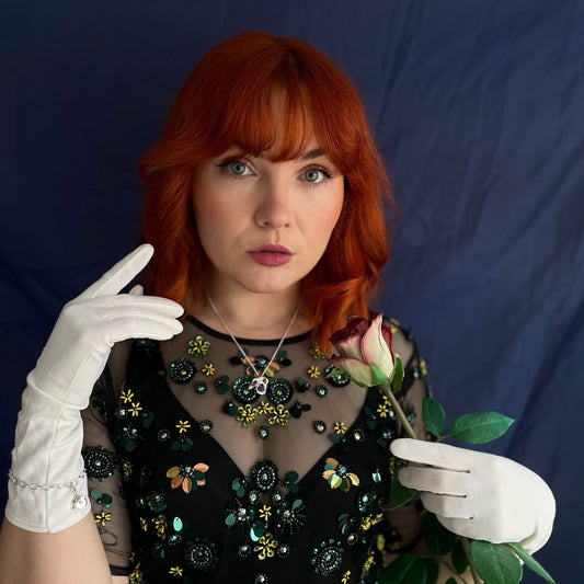 Model wearing the Phantom of the Opera Mask Necklace in sterling silver, holding a single red rose – a romantic tribute to the iconic musical and its timeless story