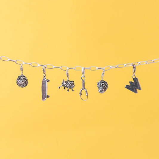 Handcrafted sterling silver Beano Charm Bracelet worn on wrist – features miniature skateboard, slingshot, and Gnasher charms, inspired by the beloved comic book characters.