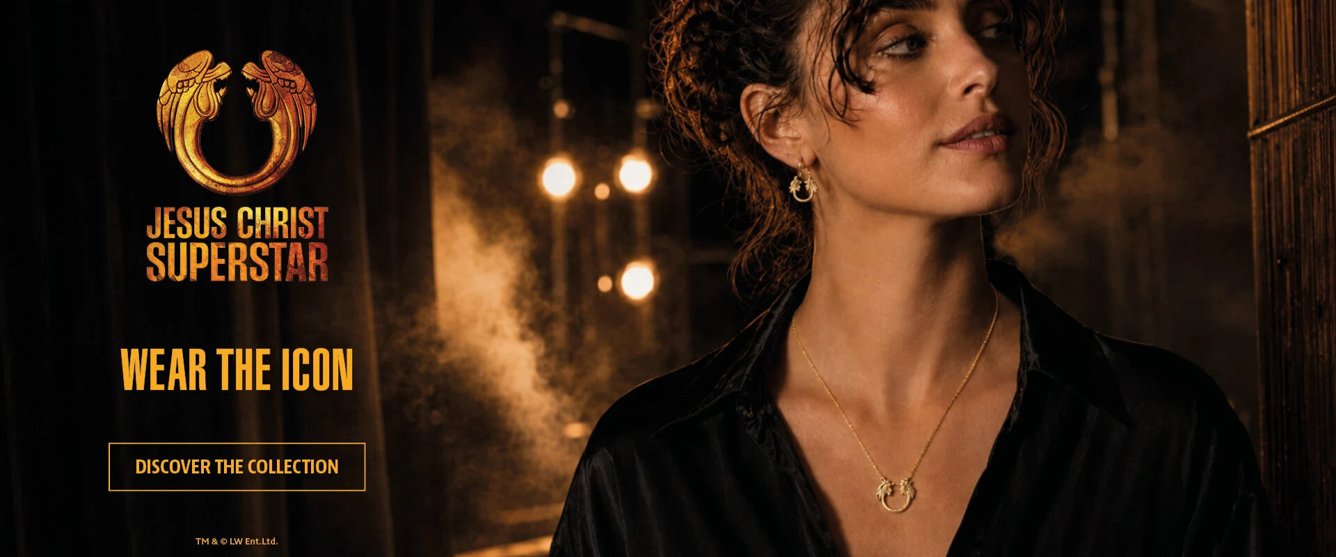 Jesus Christ Superstar gold jewellery collection banner featuring a model wearing the pendant necklace and hoop earrings, with the show’s iconic emblem in a dramatic theatre-inspired setting.
