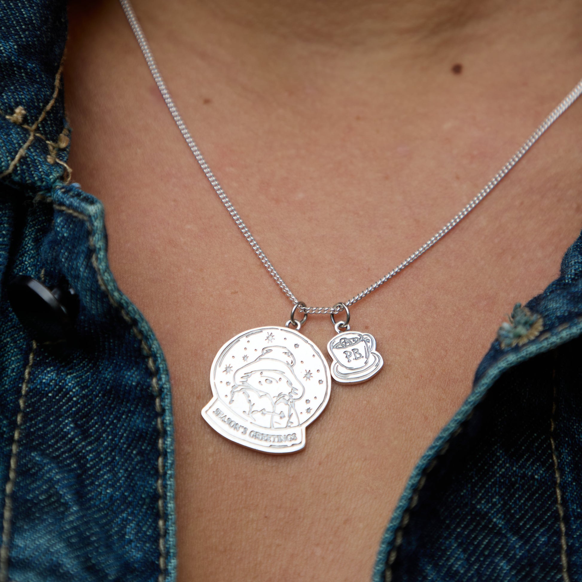 Licensed to Charm sterling silver Paddington snow globe necklace worn on a model, layered with mini PB charm, shown against a denim jacket. Perfect Christmas gifting jewellery.