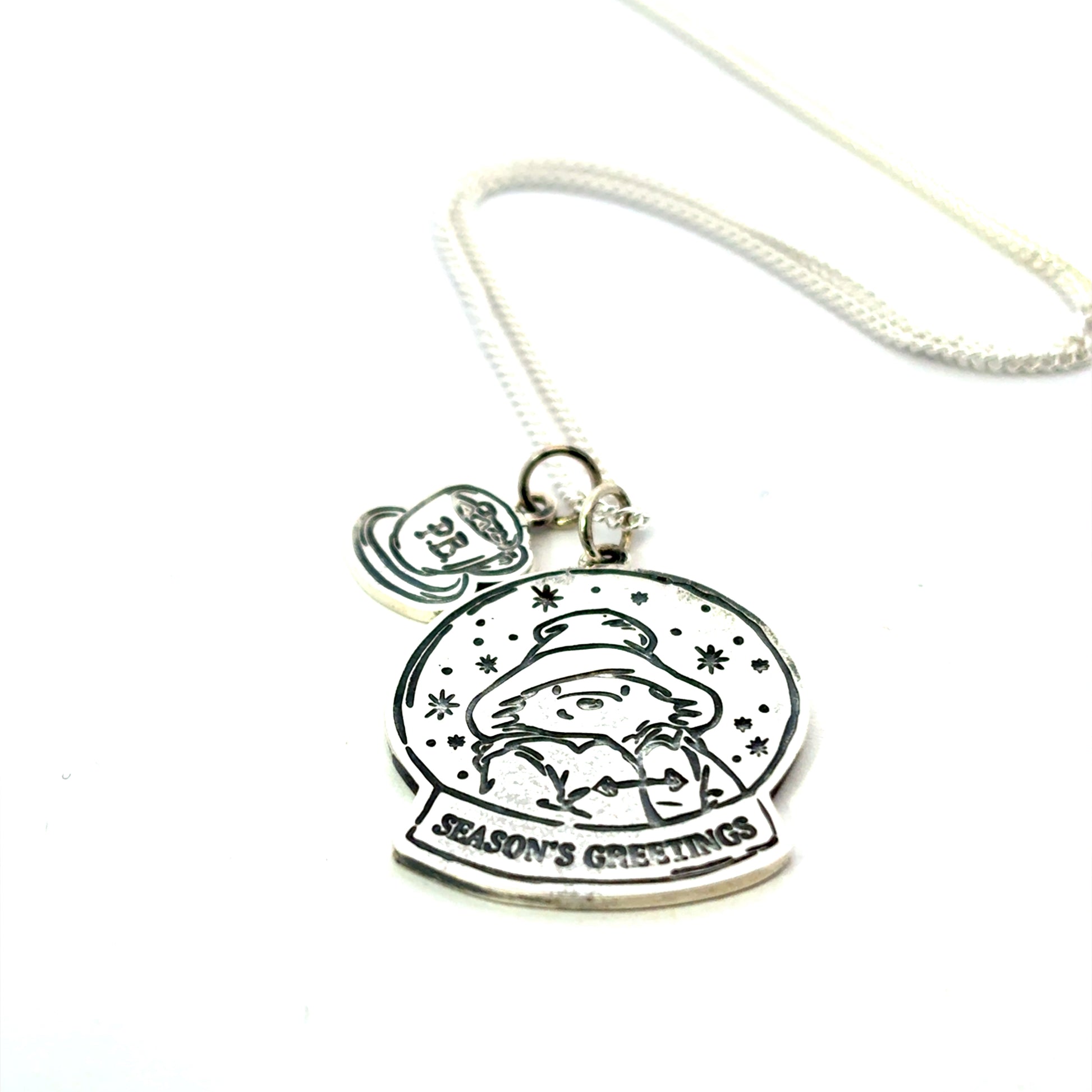 Licensed To Charm Paddington Christmas snowglobe necklace in sterling silver with hot chocolate flat lay  with 'Season's Greetings' text on a white background