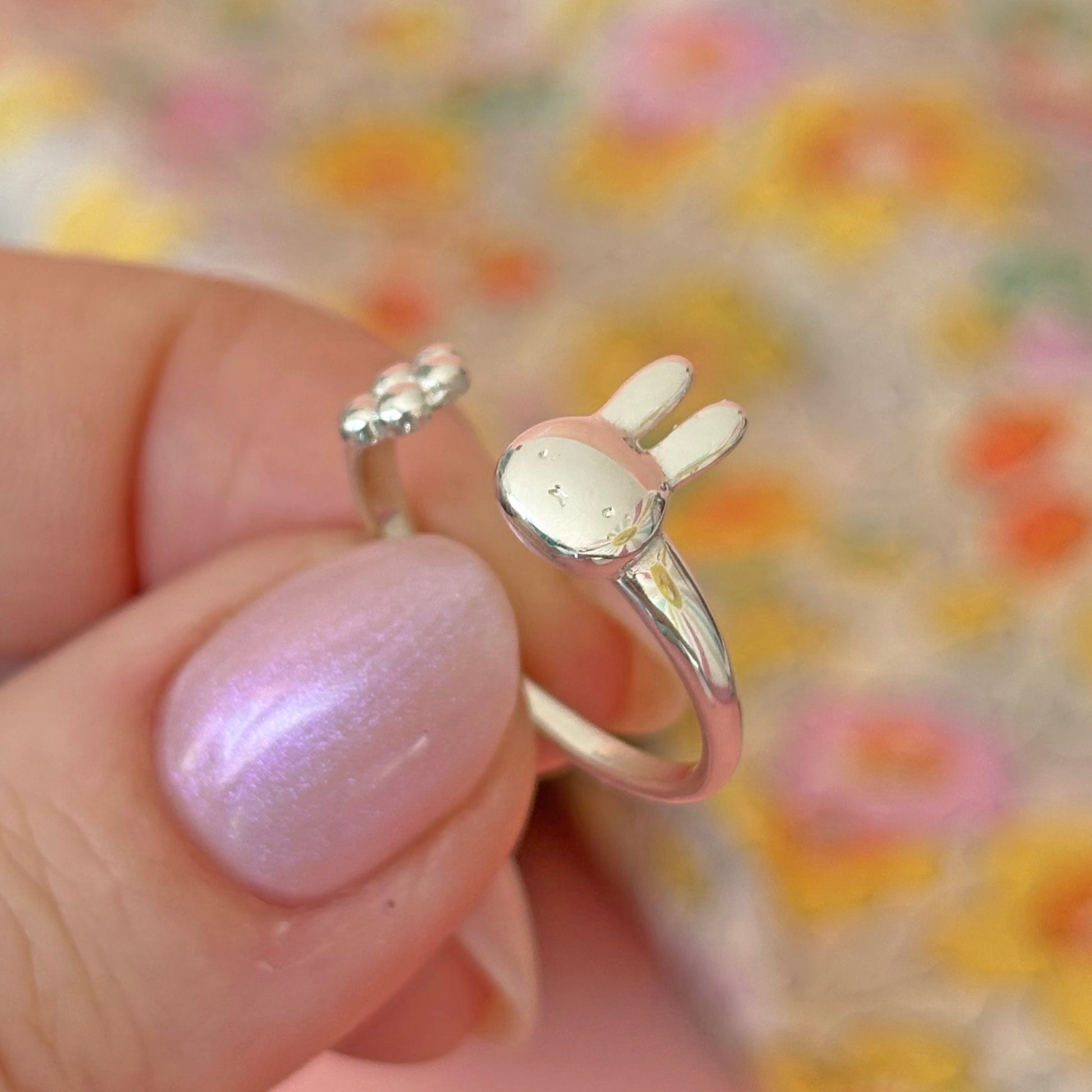 Licensed To Charm Sterling Silver Miffy ring with a rabbit design held by a hand against a colourful floral background