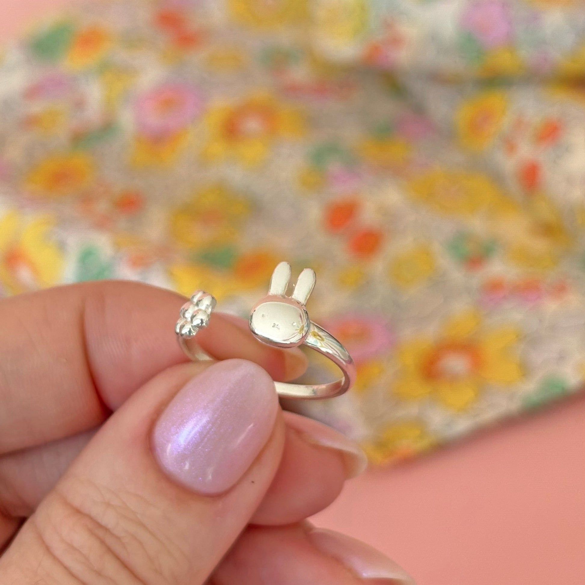 Licensed To Charm sterling silver bunny-shaped ring held by a hand with pink nail polish against a floral background