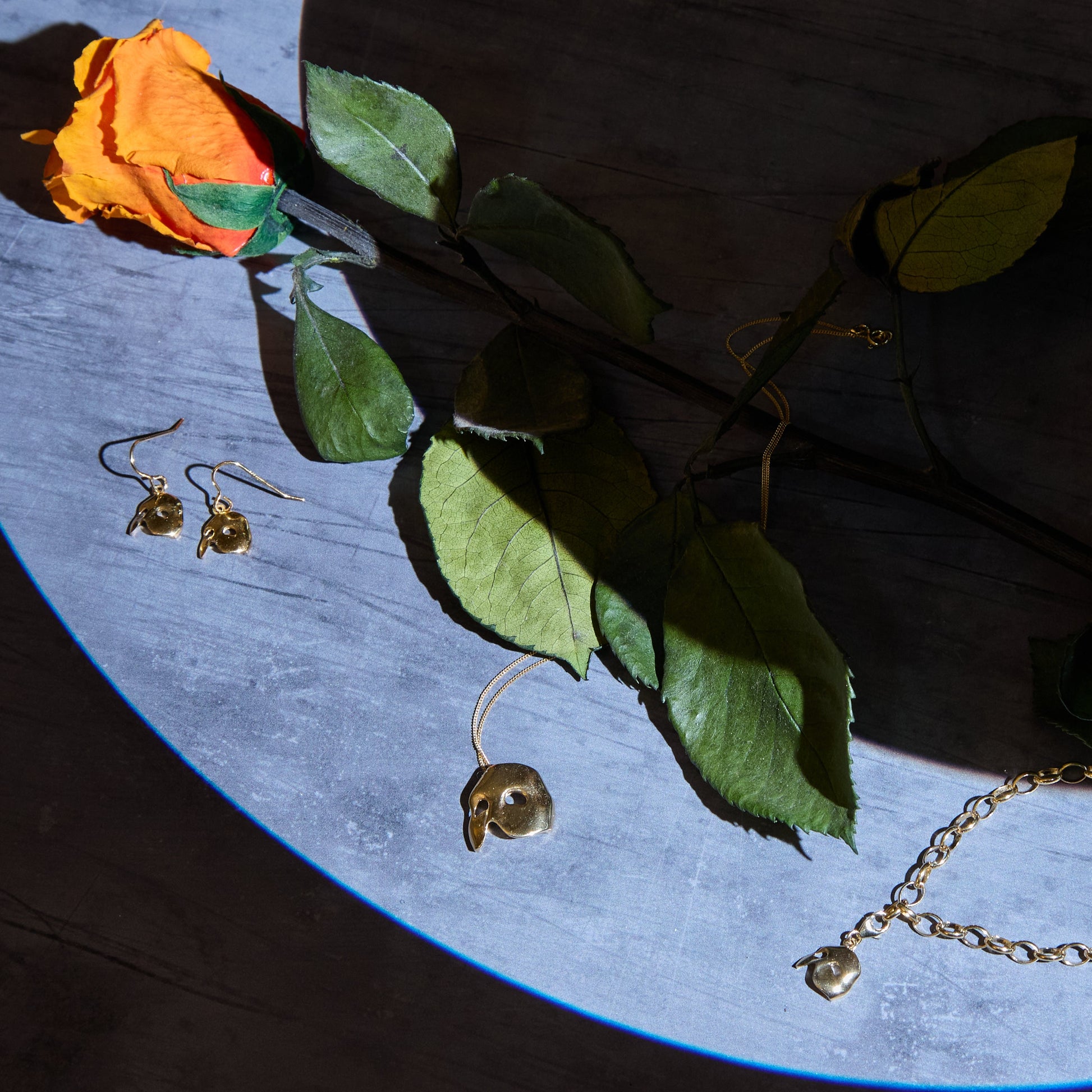 18ct Gold Vermeil jewellery including earrings and a necklace on a blue surface with a rose.