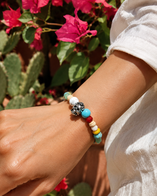 Frida Kahlo Beaded Sugar Skull Stretch Bracelet worn on a wrist in a sunlit garden with pink bougainvillea and a cream linen sleeve.