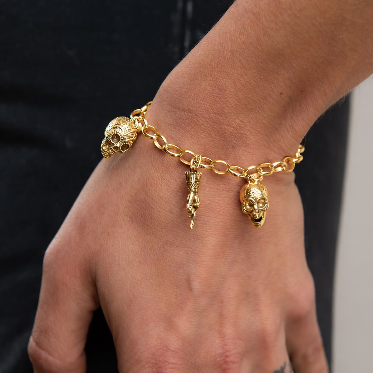 Frida Kahlo 18ct gold vermeil charm bracelet worn on a wrist, featuring two detailed skull charms and a pointing hand charm.