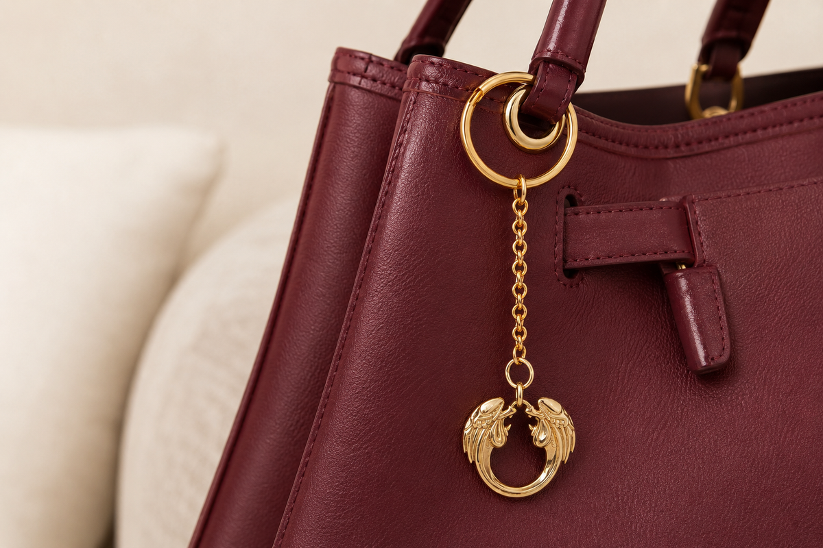 Maroon handbag with a gold jesus christ superstar bag charm on a beige background