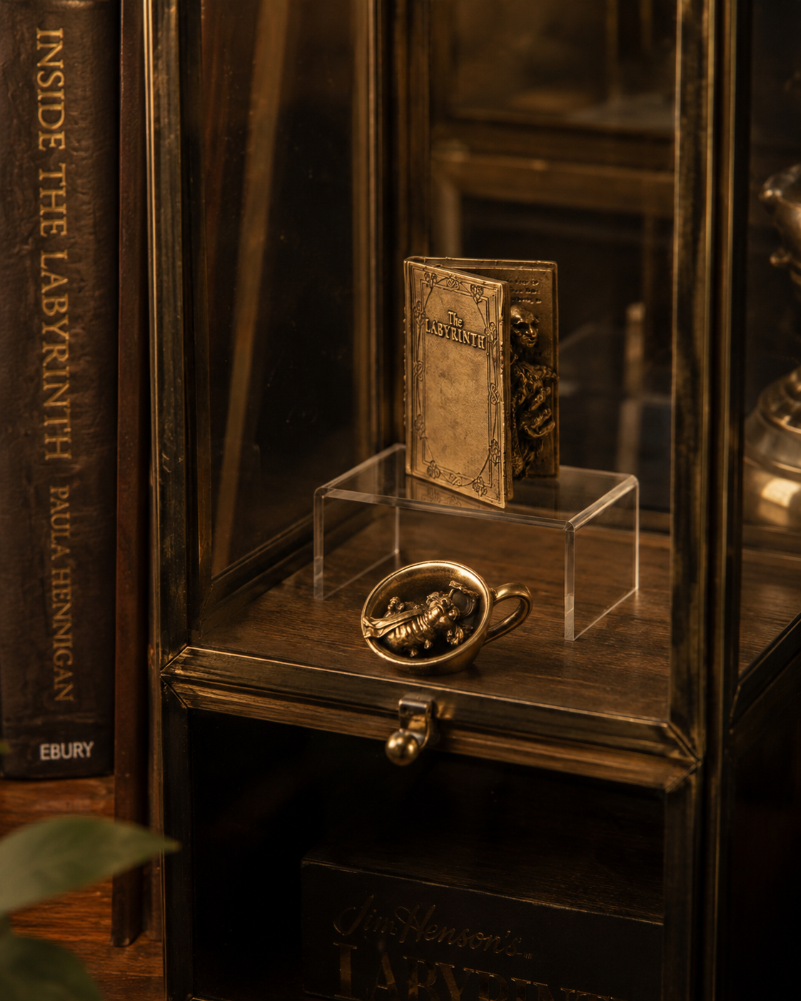 Labyrinth Character Book and Worm in a Cup bronze miniatures displayed inside a glass collector’s cabinet.
