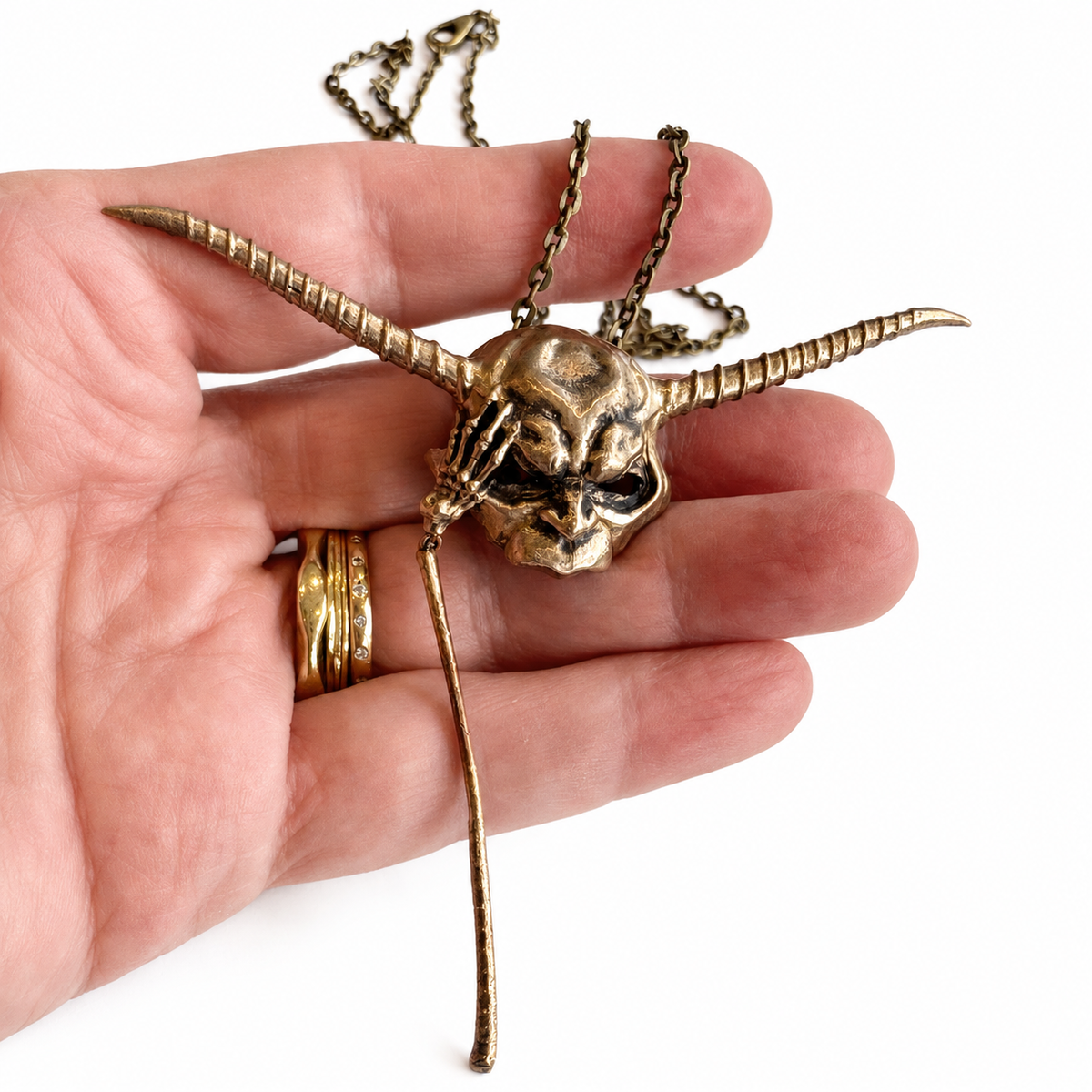 Goblin King mask bronze necklace held in a hand to show its detailed design and true scale.