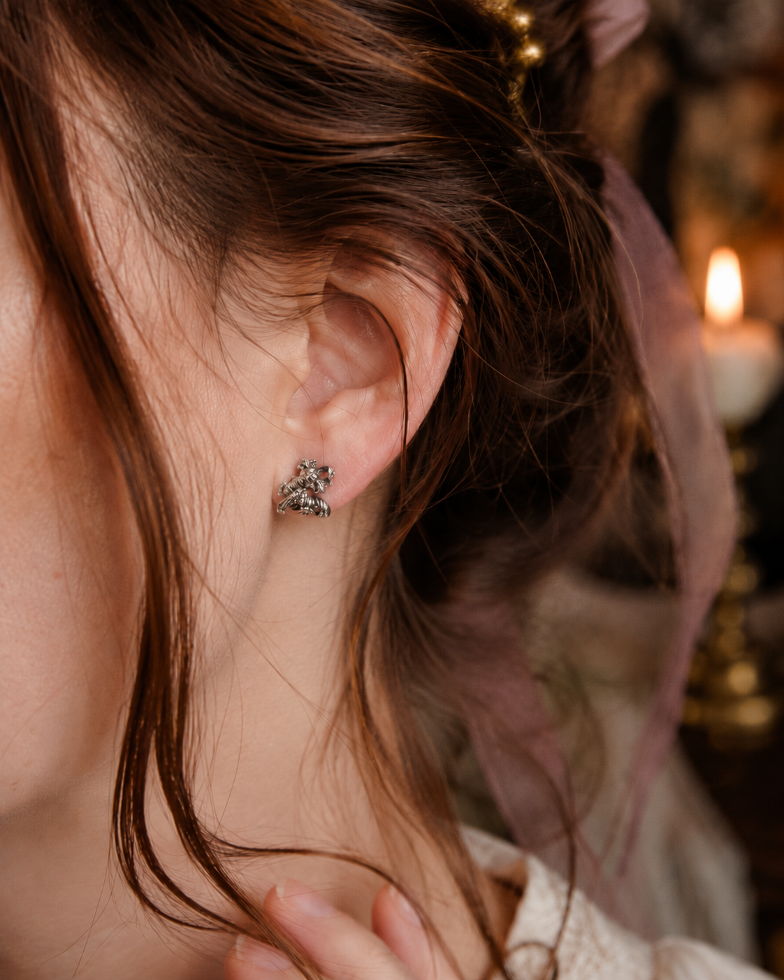 A close-up of a person's ear wearing a labyrinth-worm-stud-earrings  against a softly blurred warm indoor background.