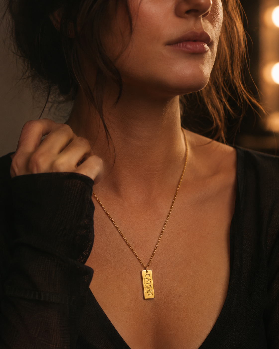 Model wearing the Licensed To Charm CATS Number Plate Necklace in Gold Plate, styled as a delicate vertical tag necklace with dark theatre-inspired fashion.