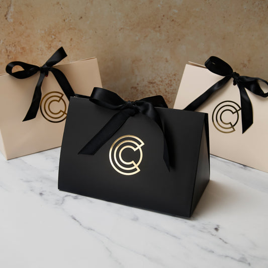 Licensed To Charm gift packaging with black and cream branded gift bags tied with black ribbon