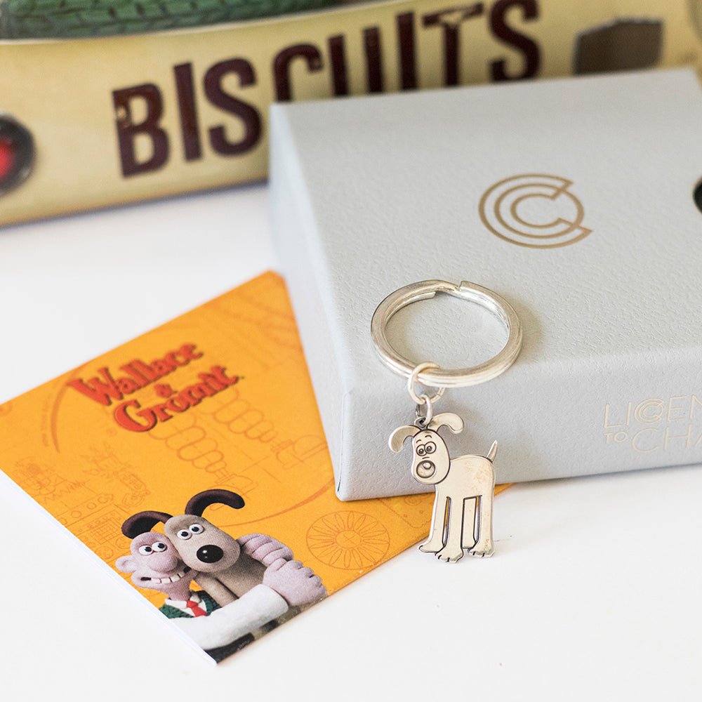 Licensed to Charm Standing Gromit keyring displayed with a Wallace & Gromit biscuits backdrop