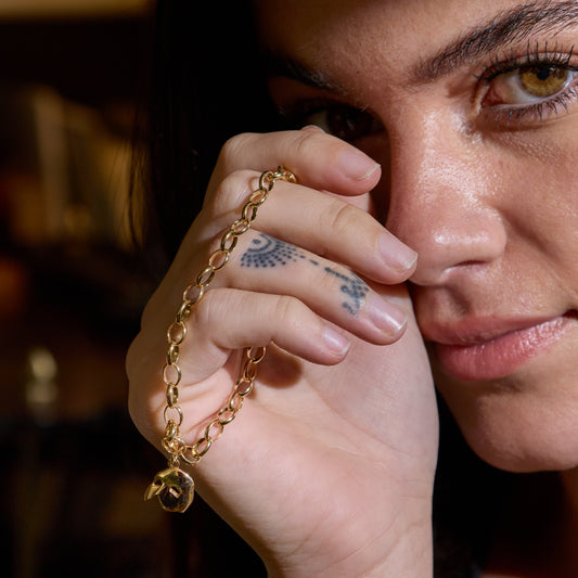 Model wearing Phantom of the Opera mask bracelet in 18ct gold vermeil, holding hand near face