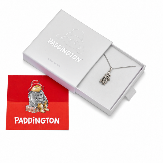 A silver Paddington pendant necklace displayed in an open white gift box next to a red Paddington card featuring the character and the brand name.