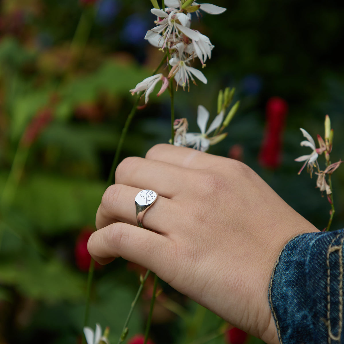 Paddington Bear sterling silver signet ring worn on a hand beside flowers in a garden.