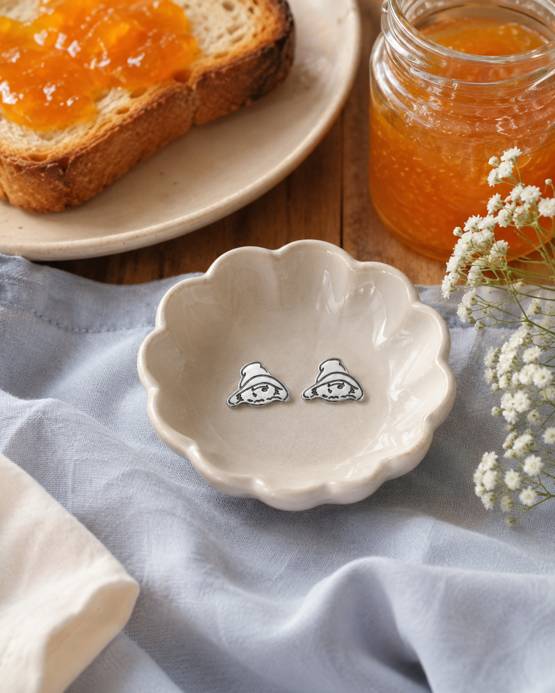 Pair of silver Paddington stud earrings styled on pale blue linen with flowers, ceramics and marmalade.