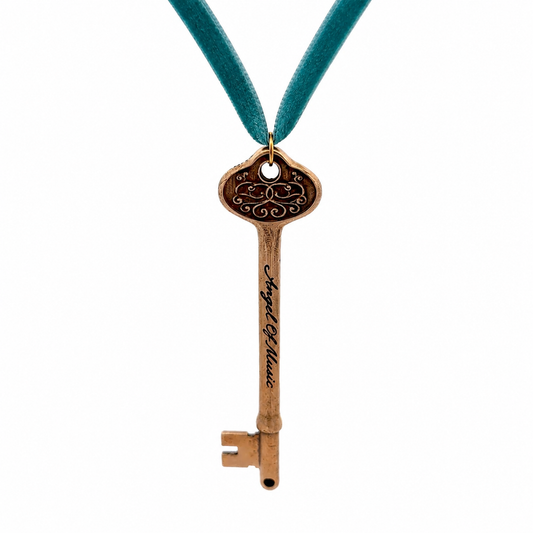 A vintage-style metal key pendant engraved with 'Angel of Music' and hanging from a teal velvet ribbon, shown against a plain white background.