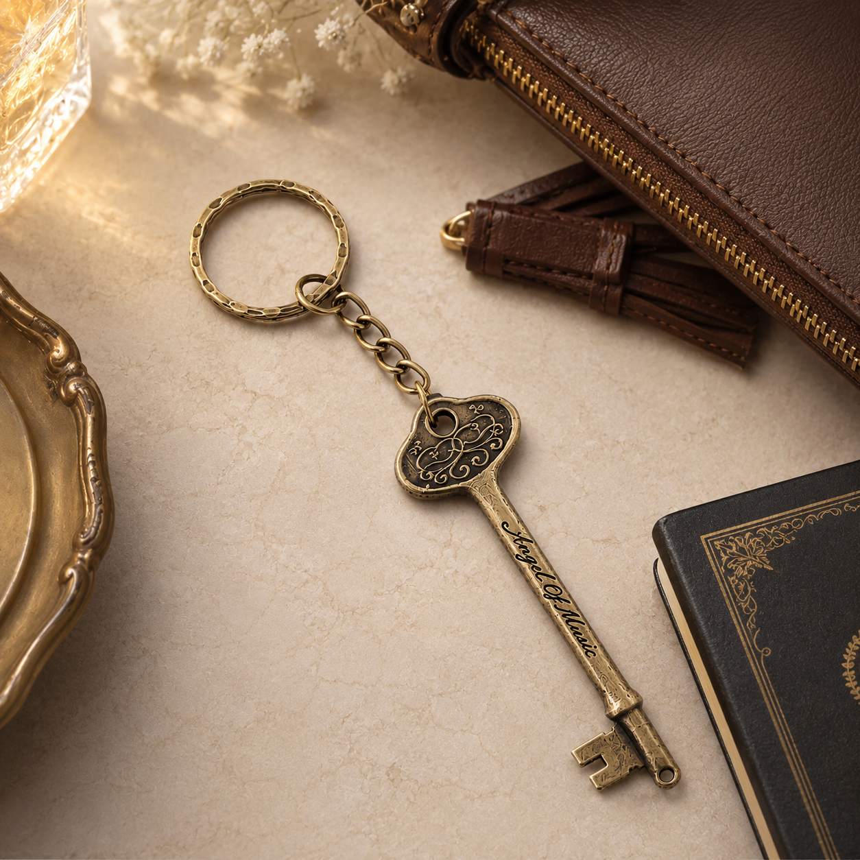 Phantom of the Opera bronze Angel of Music keyring styled beside a leather handbag and notebook.