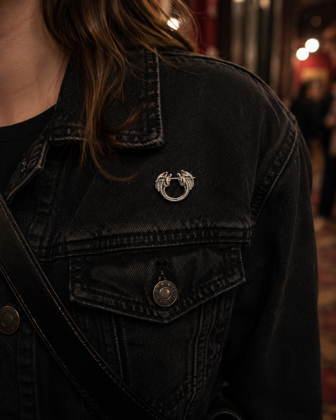 Sterling silver pin brooch worn on a black denim jacket with modern show-night styling and warm evening lighting.