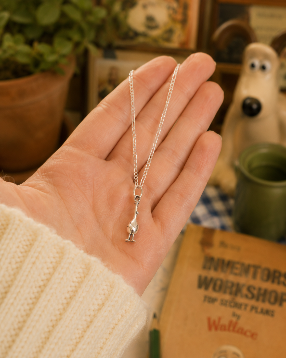 Feathers McGraw sterling silver necklace held in hand in a cosy Wallace & Gromit-inspired lifestyle setting.